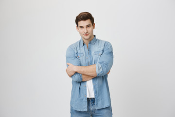 Fototapeta premium Attractive young sportsman with beautiful eyes, confident expression and crossed hands near white background. Artist just finished his painting, looking with satisfaction, enjoying result