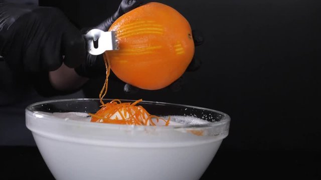 Slow motion of citrus zester grating peeling orange peel, oils spraying against dark background