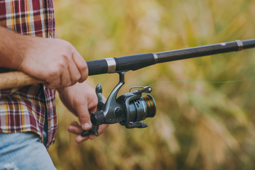 Close up A man holds and untwists a fishing reel in his hands on a blurry brown background. Lifestyle, recreation, fisherman leisure concept. Copy space for advertisement. With place for text.