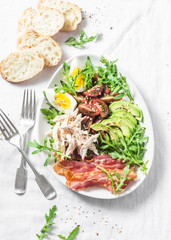 Breakfast salad bowl. Avocado, arugula, bacon, chicken, tomatoes, egg salad. Healthy balanced breakfast or snack on a light background, top view