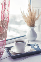 cup of coffee on a table in front of a window, the concept of breakfast and rest during work, a lifestyle of authentic, selective focus