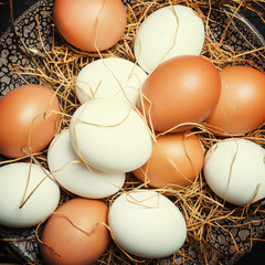 Multicolored chicken eggs with straw and branches, spring Easter composition, black background, top view