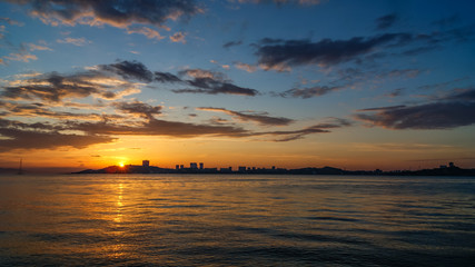 Fototapeta na wymiar Beautiful sunset on a sea, urban buildings on the bank