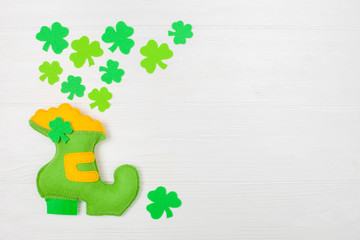 St. Patrick's Day theme colorful horizontal banner. Green leprechaun hand made shoe with gold and shamrock leaves on white wooden background. Felt craft elements. Copy space