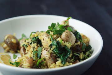 Yellow rice with mushrooms and spinach. Vegan dish. European cuisine. Vegetarian turmeric rice in the white bowl. Close up. Toned photo.