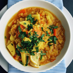 Red lentil stew with potato, carrot and turmeric. Top view. Toned photo. Healthy lunch on the round white plate. Colorful vegan dish with potato, carrot and turmeric. European cuisine. Vegetarian.