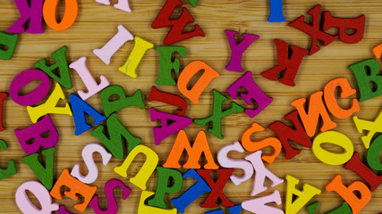 Randomly scattered colorful wooden letters on a wooden background.