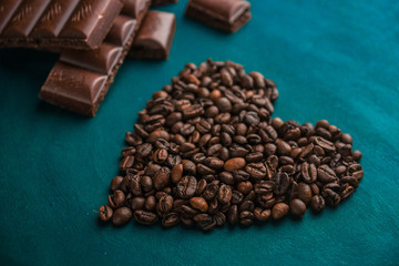 heart from fragrant coffee beans on a dark wooden background with pieces of dark chocolate