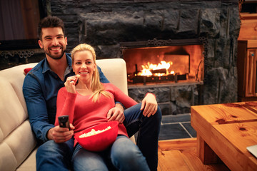 young couple eating popcorn and lying on the sofa at home watching TV