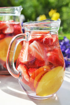 Dietary detox drink with fresh strawberry, lemon and peach fruit slices. Fruit infused water in glass jug.Summer diet.