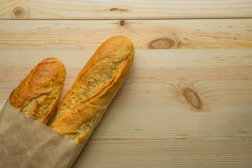 two baguettes with a golden crust in a craft pack lie on a wooden background
