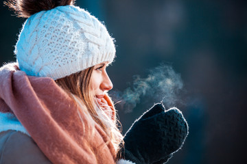 Woman breathing on her hands to keep them warm at cold winter