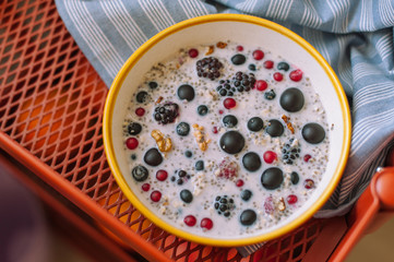 Brekfast bowl of cereal porridge and fruits on tablecloth. Grapes, blueberries, blackberris, raspberris, red currants, black currant. Healthy food concept.