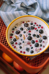 Brekfast bowl of cereal porridge and fruits on tablecloth. Grapes, blueberries, blackberris, raspberris, red currants, black currant. Healthy food concept.