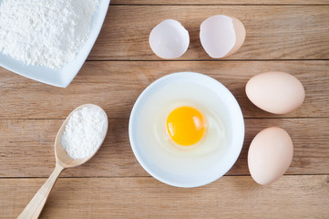 Eggs and a plate of flour on a wooden table. Ingredient for baking
