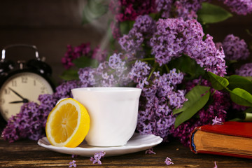 A cup of hot tea with a lemon and over a lilac flowers backdrop. Good Morning Hello Spring concept