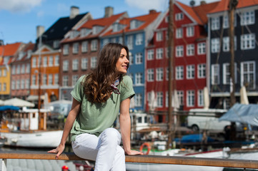Fototapeta na wymiar Young tourist woman, sitting at the Nyhavn harbor pier Copenhagen, Denmark. Visiting Scandinavia, famous European destination.