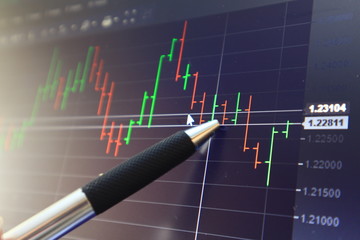 Pen point on screen with background bar chart trading.