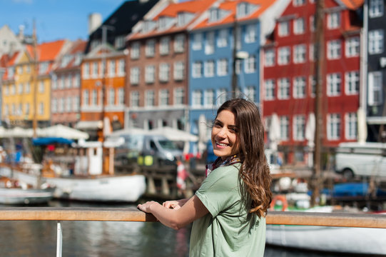 Happy young tourist woman sitting at the Nyhavn harbor pier Copenhagen, Denmark. Visiting Scandinavia, famous European destination.