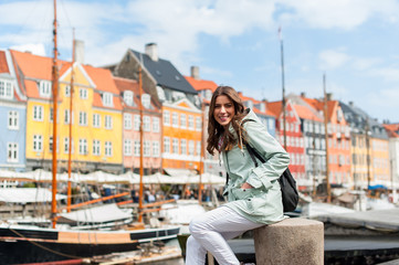 Happy young tourist woman with backpack at Copenhagen, Nyhavn, Denmark. Visiting Scandinavia,...