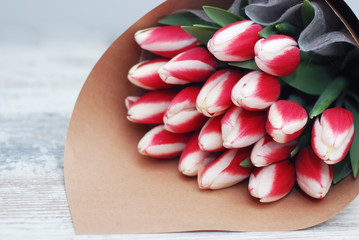Flower Bouquet with Red and white tulips in craft paper against the grey wall, close up. Copy Space for Text.