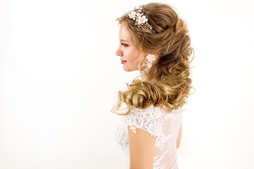 young blonde girl in a white wedding dress and jewelry in hairstyle  with big curls smiling like angel on a white wall background portrait