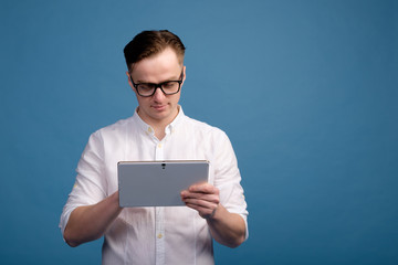 handsome white man in glasses wearing white shirt use tablet, blue background, copy space