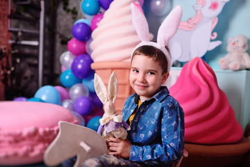 Fototapeta na wymiar baby boy with rabbit ears with easter bunny in hands smiling sitting on wooden horse