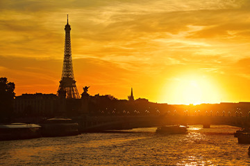 Sunset view of Paris with the Eiffel Tower and the Pont Alexandre III bridge over the river Seine with picturesque sky and a boat moving under the bridge, France