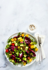 summer bright fresh salad of cherry tomatoes, avocado and radicchio leaves on a white marble table. concept of healthy eating. copy space