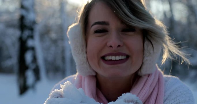 Portrait of beautiful happy girl blowing snow in frosty winter park. Outdoors. Flying snowflakes, sunny day. backlit. Joyful beauty woman having fun in winter park.