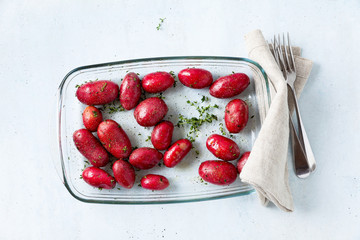 raw red potatoes in oil with spices on a resistant oven tray or Glass Oven Dish, ready to be baked in the oven