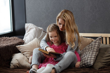 Mother and daughter sitting on the bed in an embrace and reading a book