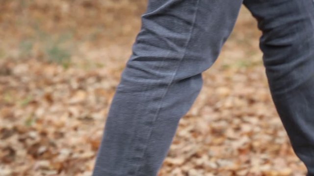 Woman in jeans and boots walking in the woods, on a carpet of dry leaves.