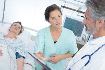 doctor and nurse with clipboards visiting patient at hospital ward