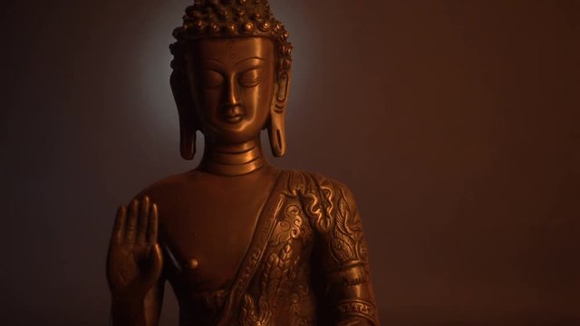 Statuette of Buddha on the black background. Moving of the light.
