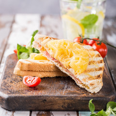 Hot fresh hawaii toast sandwich with ham, pineapple, tomato and cheese on wooden board. Healthy summer food concept with free space for text.