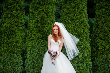 Obraz na płótnie Canvas Beautiful smiling red hair bride with wedding bouquet