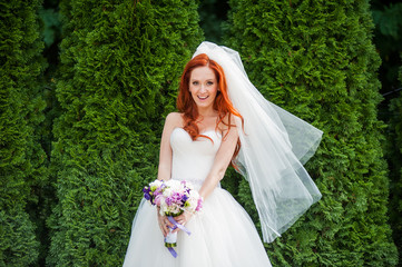 Bride with flowers in hand outdoors in summer or winter. The bride is nervous before the wedding. Bride holding a perfume. nice wedding bouquet in bride's hand. Girl is holding beautiful bright weddin