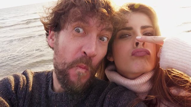 Cute happy couple on the beach at sunset making funny faces selfie video closeup