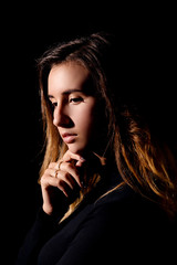 A young brunette woman with long hair is holding her hand under the chin and is looking down on a black background close-up