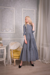 Blonde girl in long grey retro dress stands gracefully in vintage interiors
