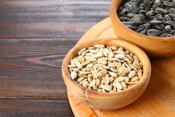Black peeled and unpeeled sunflower seeds in a wooden bowl on a wooden table.