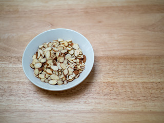 Angled shot of of porcelain bowl filled with sliced almonds on chopping block