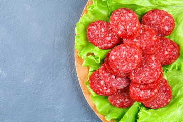 Smoked sausage, salami chopped in slices on a salad on a wooden circular cutting board on a concrete gray table.
