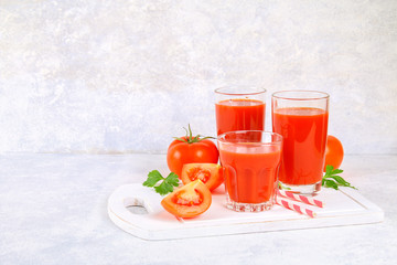 Tomato juice in glasses on a gray concrete table.