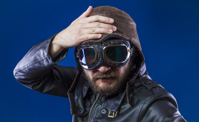Fototapeta premium pilot of the 20s with sunglasses and vintage aviator helmet. Wears leather jacket, beard and expressive faces