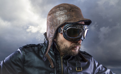 Old plane pilot on background of storm clouds with expressive face. glasses and old hat with black...