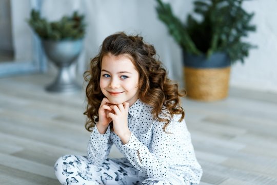 A photo of a beautiful little girl with blue eyes and brunette curly hair in studio sitting on the floor and smiling