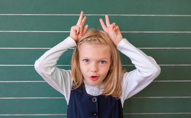 First grade pupil a girl writing on green blackboard at school lesson